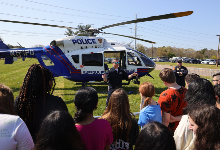 SCPD helicopter pilot speaks with CMS students with helicopter behind him.