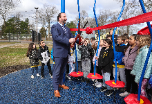 Superintendent Dr. Jordan Cox prepares to cut a red ribbon as students cheer the opening of the Wood Park playground.