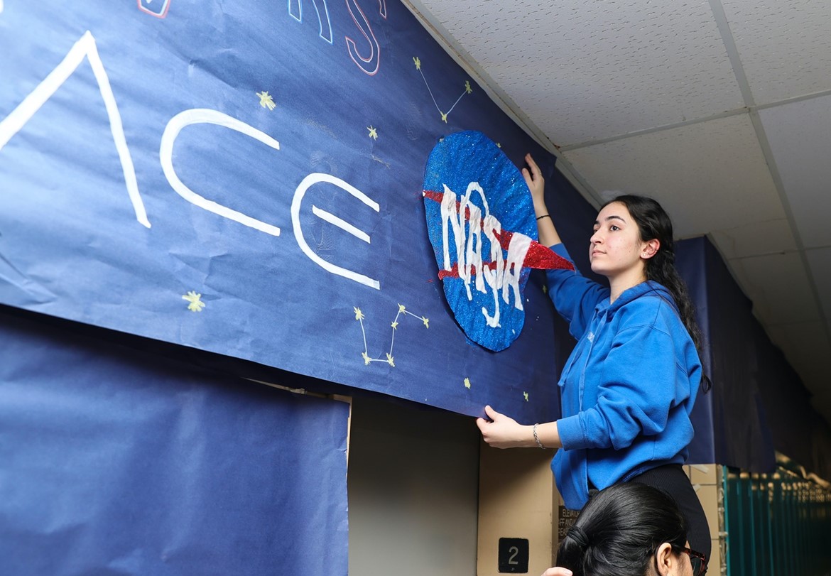 Student hangs NASA banner during hallway design contest in high school.