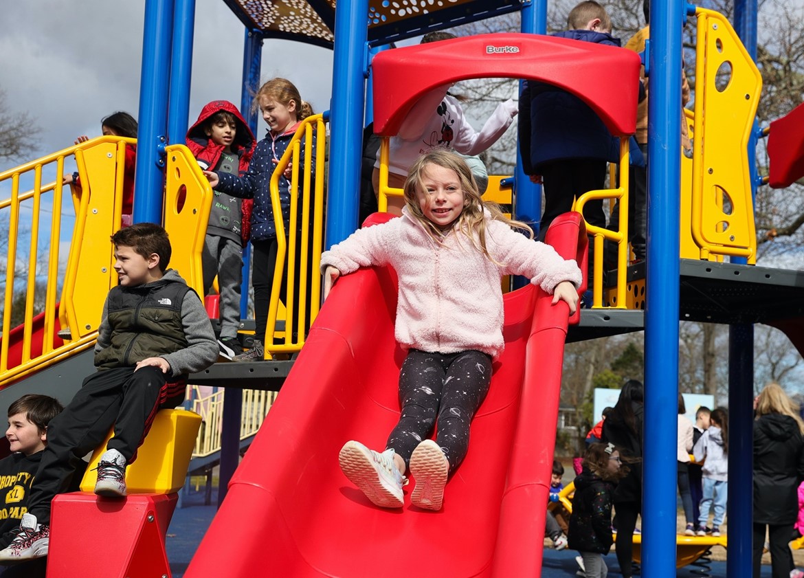 Young student on slide on playground opening day.