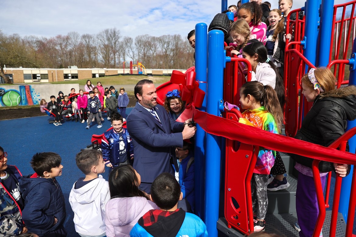 Dr. Cox cuts red ribbon at opening of Rolling Hills playground as students watch. 