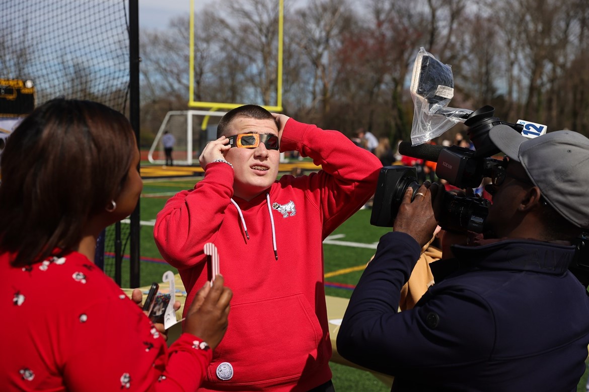 Student wearing eclipse glasses is interviewed by News 12.