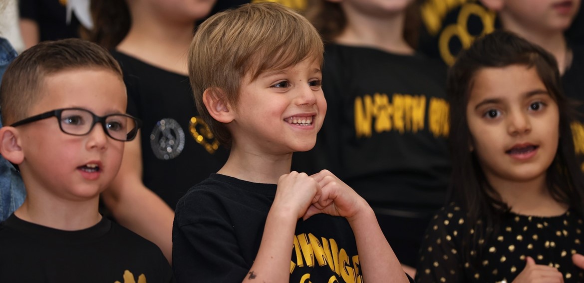 Kindergarten student smiles while with classmates during spring singing performance for parents. 