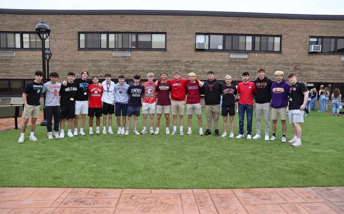 High School seniors pose in the courtyard while wearing their college sweatshirts and other apparel.