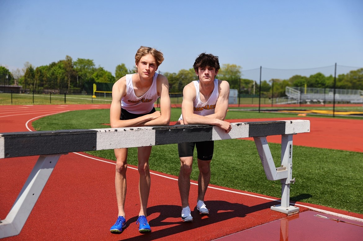 Pair of Newsday top 50 boys track athletes pose leaning on hurdle.